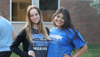 Two students smiling looking at the camera  outside of a building on campus